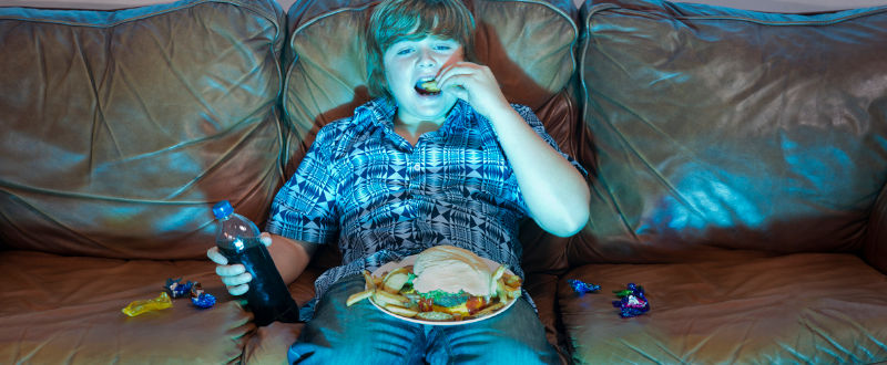 adolescente ve televisión mientras come comida chatarra