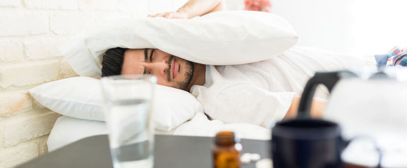 Hombre apretandose la cabeza con una almohada - resaca