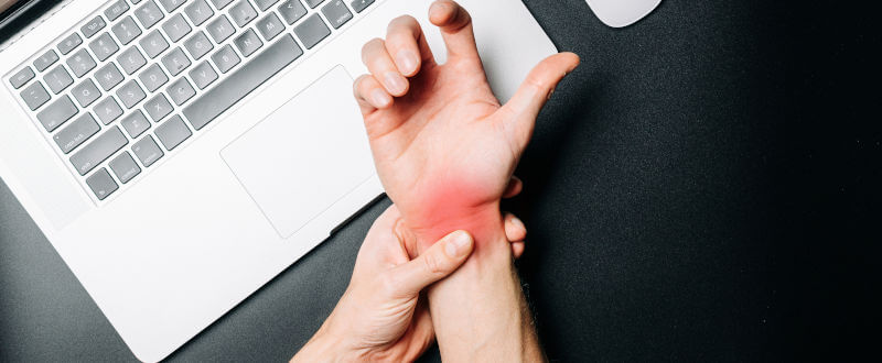 muñeca con dolor sujetada con la otra mano sobre un notebook