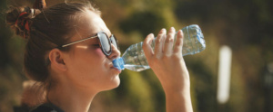 mujer con calor bebiendo de una botella con agua